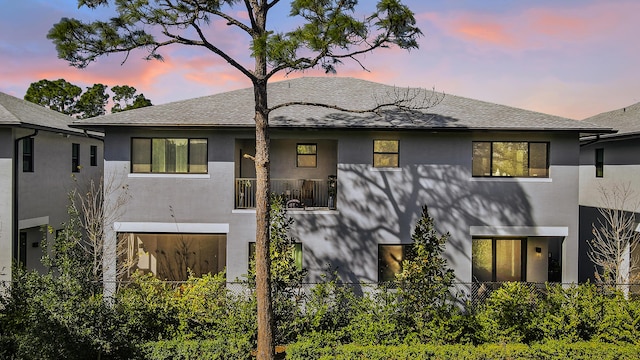 back of property at dusk with roof with shingles, fence, and stucco siding