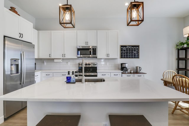 kitchen featuring decorative light fixtures, tasteful backsplash, appliances with stainless steel finishes, white cabinets, and a kitchen breakfast bar