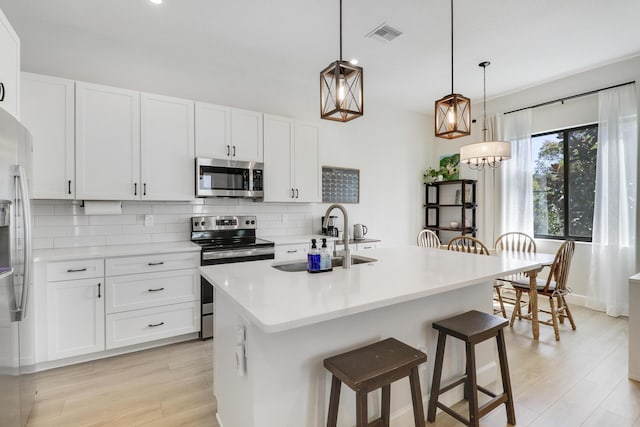 kitchen with tasteful backsplash, appliances with stainless steel finishes, white cabinetry, a sink, and a kitchen bar