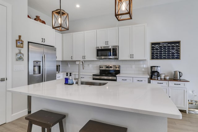 kitchen with appliances with stainless steel finishes, a sink, light wood-style floors, and decorative backsplash