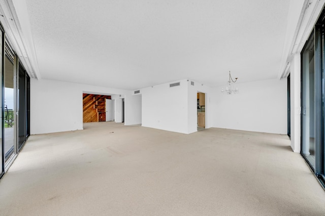 unfurnished room featuring a wall of windows, light colored carpet, a notable chandelier, and visible vents