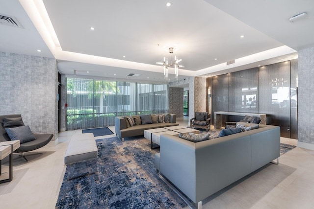 living room featuring a wall of windows, a tray ceiling, visible vents, and a notable chandelier