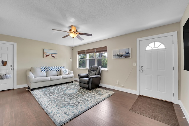 living room with dark wood-type flooring, a ceiling fan, baseboards, and a textured ceiling