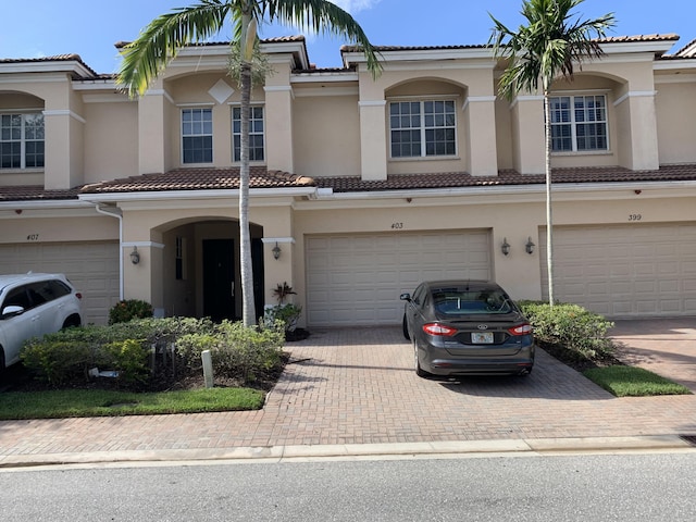 multi unit property with an attached garage, a tiled roof, decorative driveway, and stucco siding