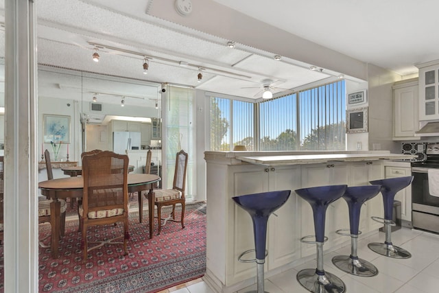 kitchen featuring light tile patterned floors, a breakfast bar, stainless steel electric range oven, white fridge with ice dispenser, and glass insert cabinets