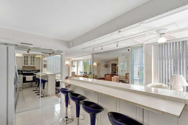 kitchen featuring light tile patterned floors, stainless steel electric range, freestanding refrigerator, a kitchen bar, and glass insert cabinets