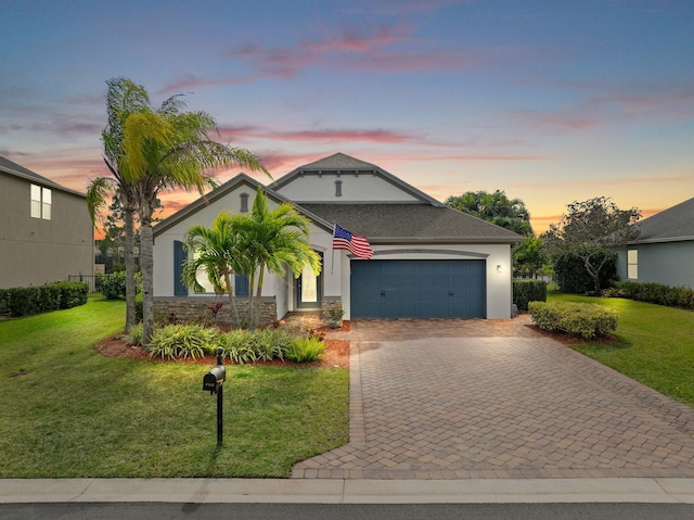 view of front facade featuring a lawn, stone siding, an attached garage, decorative driveway, and stucco siding