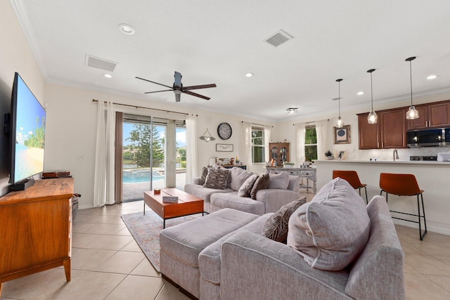 living area featuring light tile patterned floors, visible vents, a wealth of natural light, and crown molding