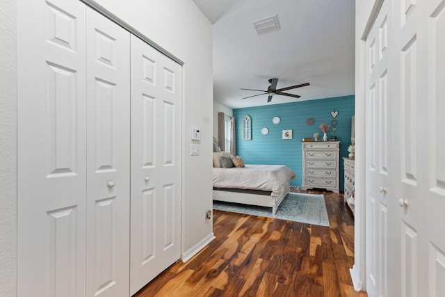 bedroom with dark wood-style flooring, a closet, visible vents, an accent wall, and ceiling fan