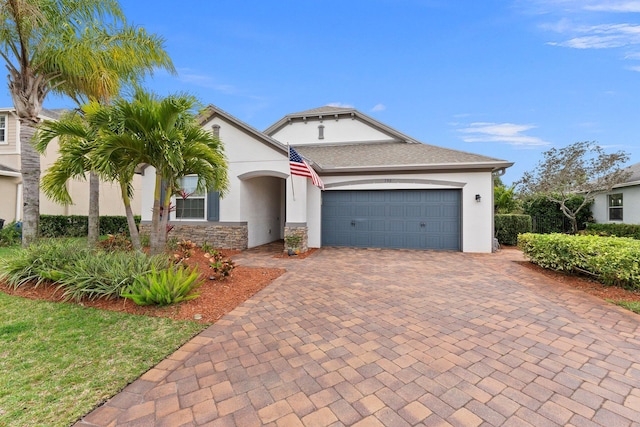 view of front of property featuring an attached garage, stone siding, decorative driveway, and stucco siding