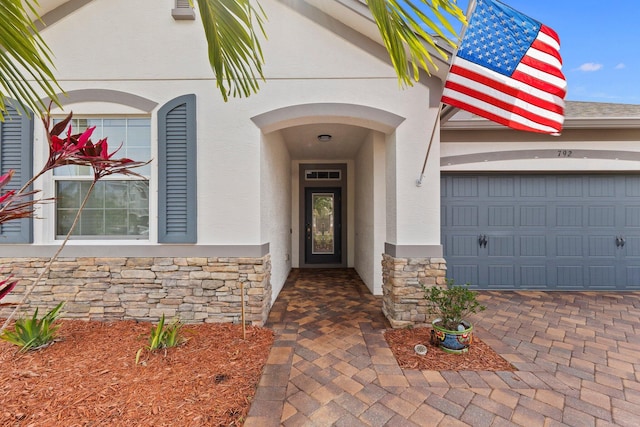 view of exterior entry with a garage, stone siding, decorative driveway, and stucco siding