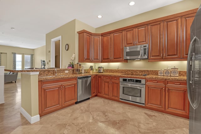 kitchen featuring stone counters, appliances with stainless steel finishes, a peninsula, and a sink