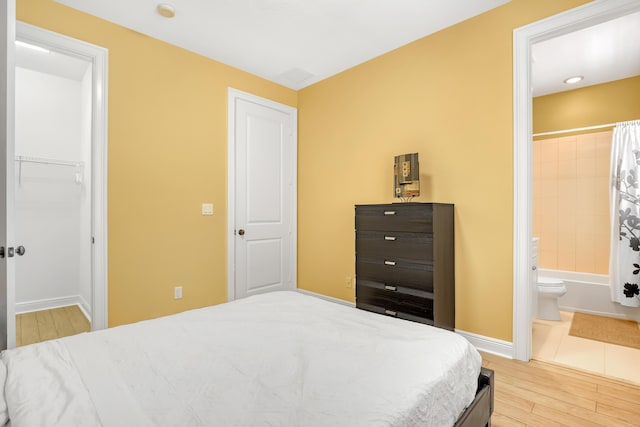 bedroom with a closet, ensuite bath, baseboards, and wood finished floors