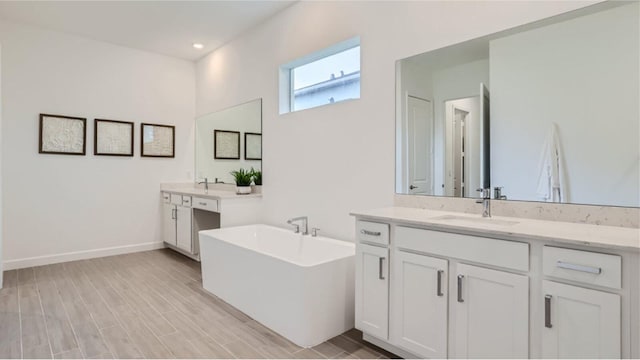 bathroom featuring baseboards, a soaking tub, wood finished floors, a sink, and two vanities