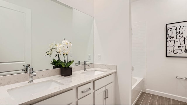 full bath featuring double vanity, wood tiled floor, baseboards, and a sink