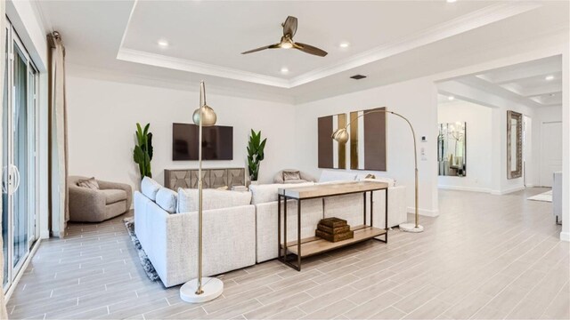 living room featuring light wood finished floors, ornamental molding, a raised ceiling, and recessed lighting