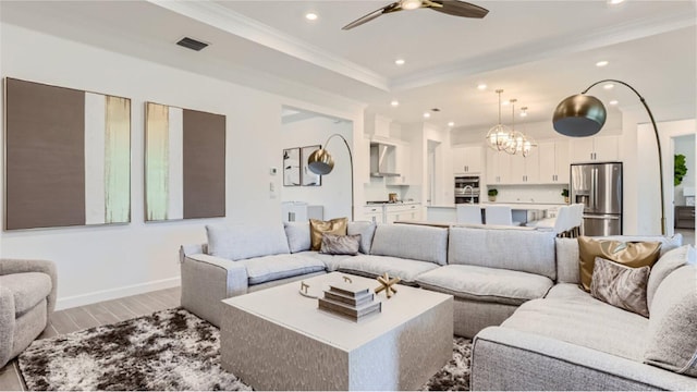 living room featuring recessed lighting, visible vents, crown molding, light wood-type flooring, and ceiling fan with notable chandelier