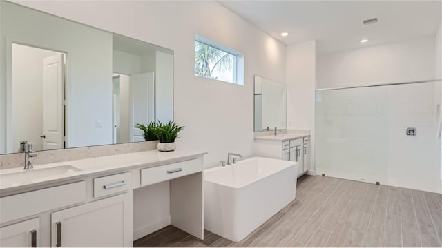 bathroom featuring wood tiled floor, two vanities, a tile shower, and a sink