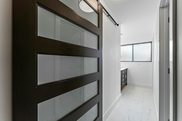 hall featuring marble finish floor, a barn door, and baseboards