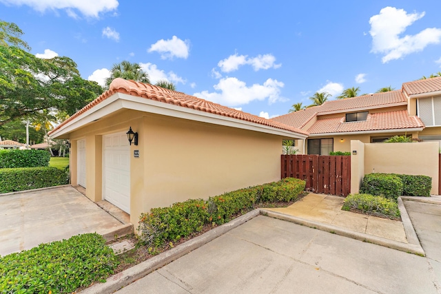 view of home's exterior featuring a garage, fence, a tiled roof, and stucco siding