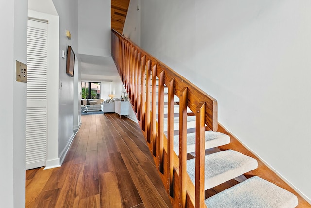 staircase with a towering ceiling, baseboards, and wood finished floors