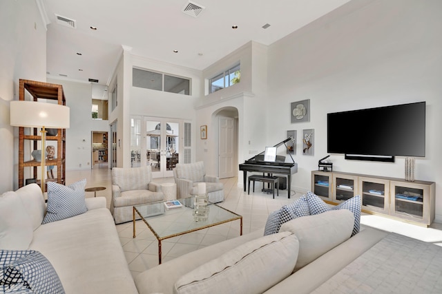 tiled living area with visible vents, arched walkways, baseboards, and a towering ceiling