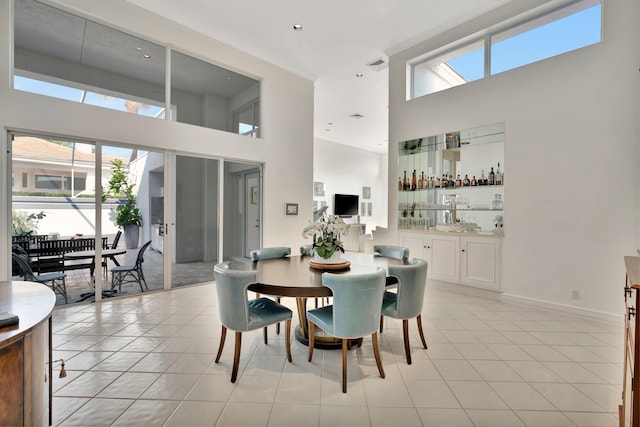 dining room featuring visible vents, baseboards, a high ceiling, light tile patterned floors, and bar area