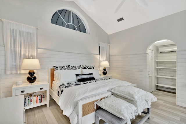 bedroom with visible vents, a wall unit AC, high vaulted ceiling, and light wood finished floors