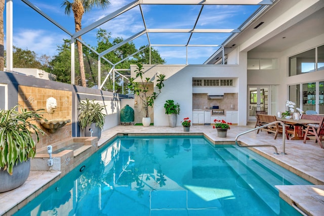 outdoor pool with a patio area, glass enclosure, and exterior kitchen