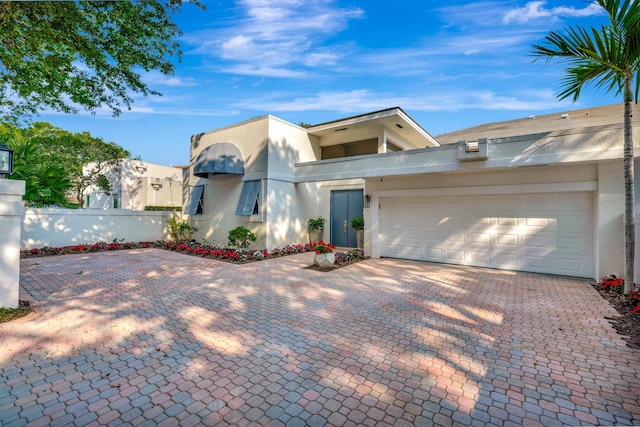 view of front of home featuring stucco siding, decorative driveway, an attached garage, and fence