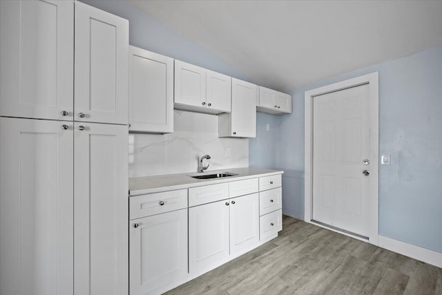 kitchen with light countertops, light wood-style flooring, decorative backsplash, white cabinets, and a sink