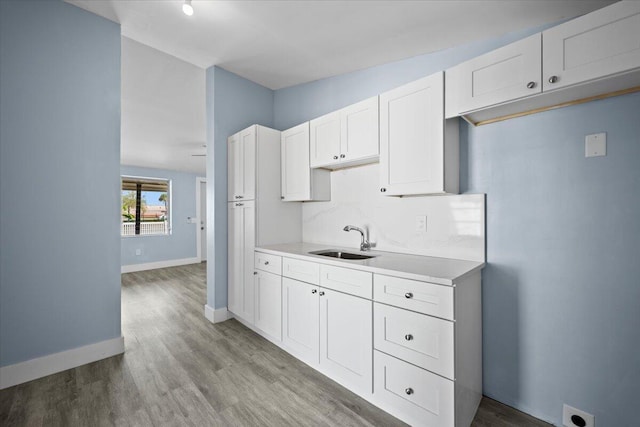 kitchen with a sink, white cabinetry, light countertops, backsplash, and light wood finished floors