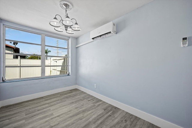 empty room featuring a wall unit AC, baseboards, a notable chandelier, and wood finished floors