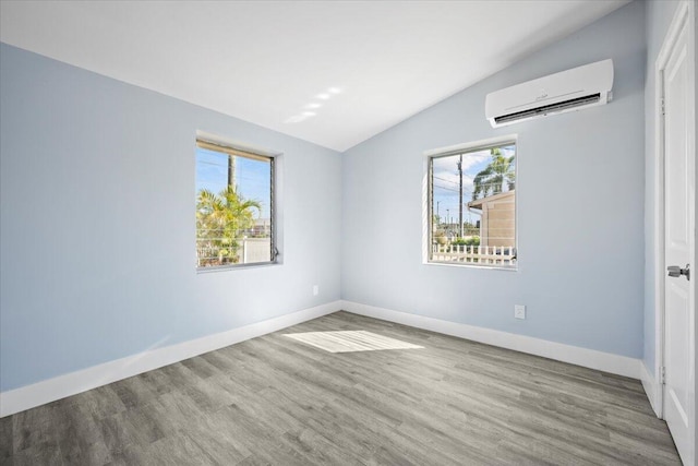 spare room with vaulted ceiling, a wall mounted air conditioner, wood finished floors, and baseboards