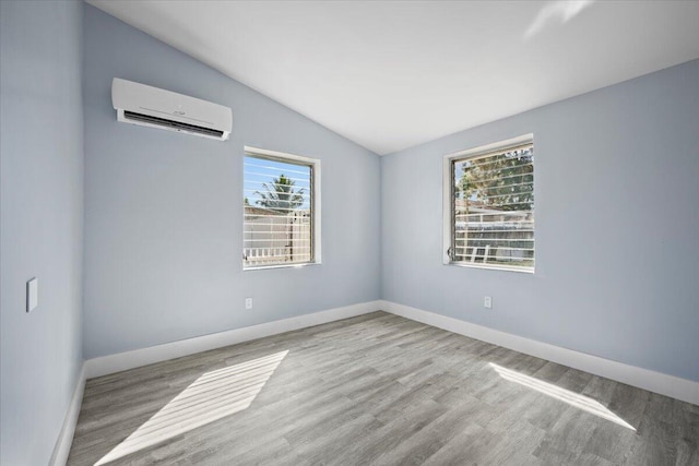 unfurnished room featuring lofted ceiling, baseboards, an AC wall unit, and wood finished floors