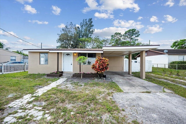 view of front of house featuring stucco siding, concrete driveway, fence, an attached carport, and a front lawn