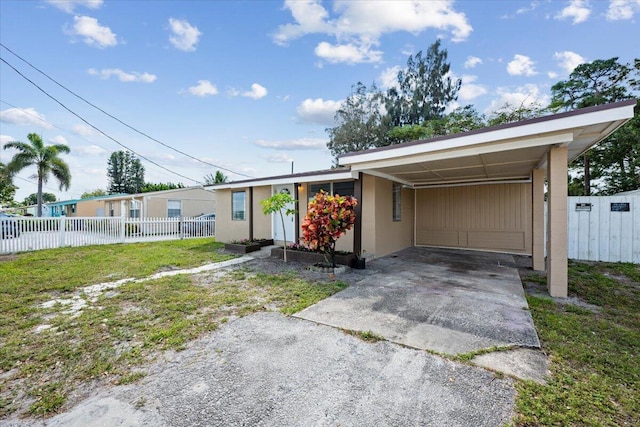 view of front of house with stucco siding, a front yard, fence, an attached carport, and driveway