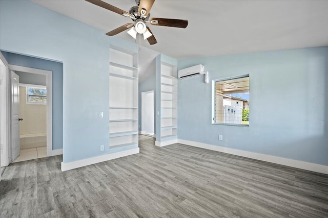 unfurnished bedroom featuring wood finished floors, multiple windows, baseboards, and a wall mounted AC