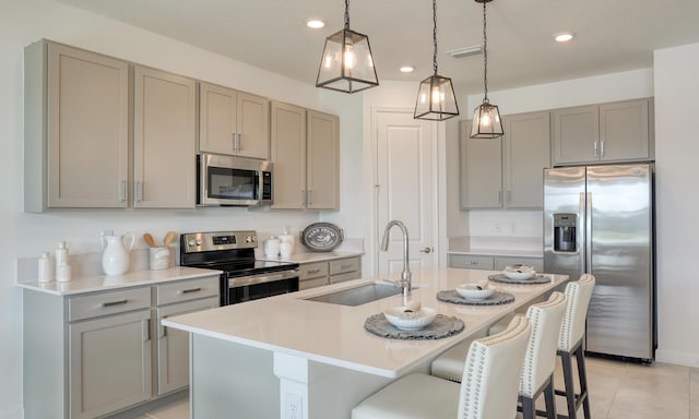 kitchen with a kitchen breakfast bar, stainless steel appliances, a sink, and gray cabinetry