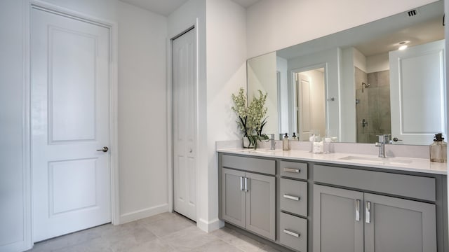 bathroom featuring a tile shower, double vanity, a sink, and baseboards