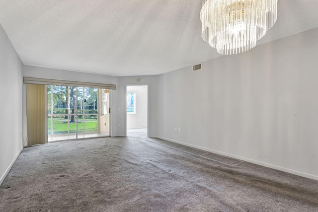 carpeted empty room featuring a textured ceiling, baseboards, visible vents, and a notable chandelier