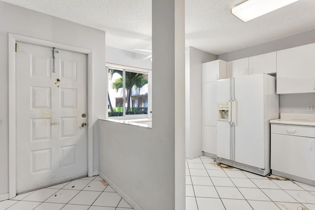 kitchen featuring baseboards, light countertops, a textured ceiling, white fridge with ice dispenser, and white cabinetry