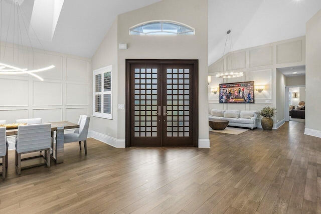 entryway with french doors, light wood-style flooring, a chandelier, a decorative wall, and high vaulted ceiling