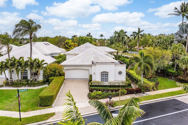 view of front of house with a front lawn, a tiled roof, driveway, an attached garage, and stucco siding