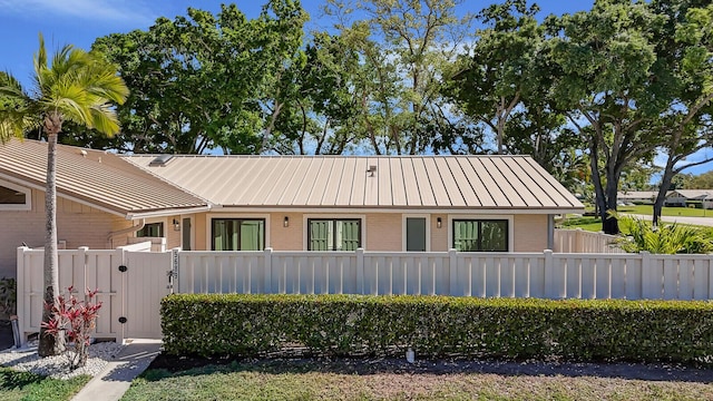 ranch-style home featuring a standing seam roof, fence, brick siding, and metal roof