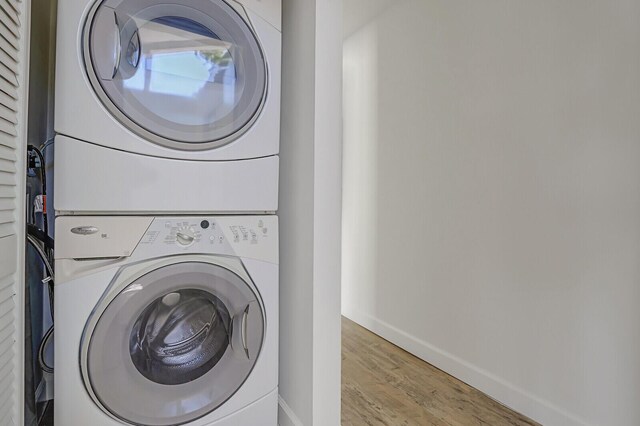 laundry area with laundry area, stacked washer / dryer, wood finished floors, and baseboards