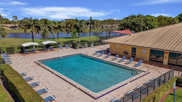 community pool with a patio, fence, a water view, and a lawn