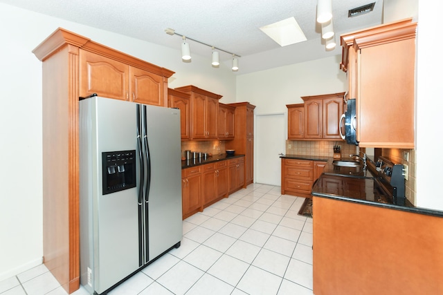 kitchen with light tile patterned flooring, stainless steel appliances, a skylight, backsplash, and dark countertops