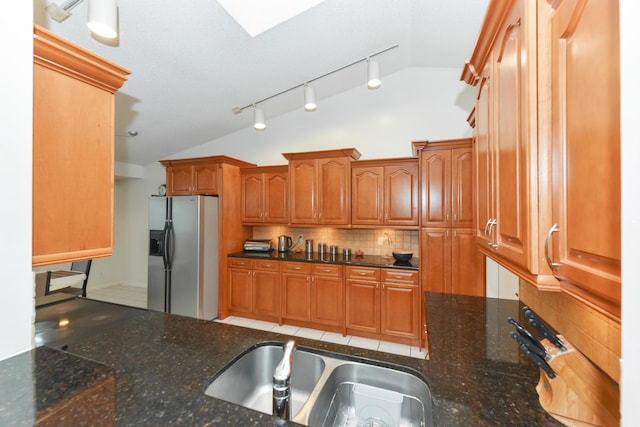 kitchen with dark stone countertops, a sink, vaulted ceiling, stainless steel refrigerator with ice dispenser, and backsplash