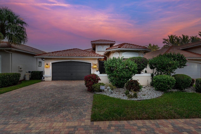 mediterranean / spanish-style home with a garage, a tiled roof, decorative driveway, and stucco siding